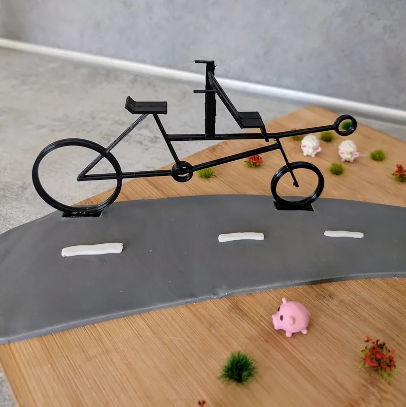 Maquette d’un vélo imprimée en 3D, posée sur une route miniature avec des petits cochons